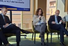 Antiriciclaggio nel gioco, Poso (ADM): “Riduzione del contante aiuta a controllare i giocatori, proposte nuove modalità di riscossione nelle VLT” Woman speaks into a microphone during a panel discussion, flanked by two men reviewing papers.