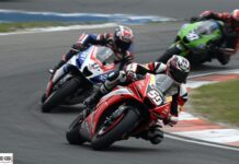 Scommesse antepost Motogp: per Lottomatica Bezzecchi è avanti a Marquez Motorcycle race with three riders leaning into a curve on a racetrack. Foreground bike is red, other bikes blue and green in the background.