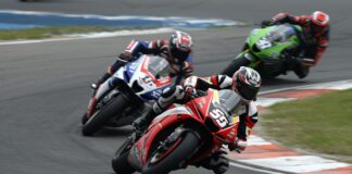 Scommesse antepost Motogp: per Lottomatica Bezzecchi è avanti a Marquez Motorcycle race with three riders leaning into a curve on a racetrack. Foreground bike is red, other bikes blue and green in the background.