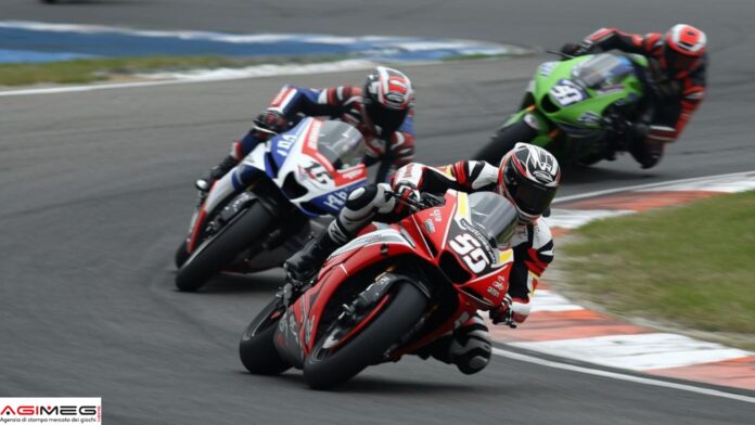 MotoGp Motorcycle race with three riders leaning into a curve on a racetrack. Foreground bike is red, other bikes blue and green in the background.