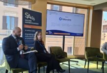 Salone Antiriciclaggio: il contributo di Dataware nello sviluppo di dati e soluzioni per il gioco. Tutti gli interventi Two presenters sit on green chairs during a conference; a tall banner reads 'SALONE ANTIRICICLAGGIO' beside a large screen displaying a Dataware slide.