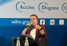 Stati Generali ADM, Taddia (CIO): “Match fixing, una delle minacce più gravi per l’integrità dello sport” Woman in a blazer speaks into a handheld microphone on a blue stage backdrop with government logos and social icons.