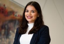 Giochi: Erika Spiteri Bailey nuova co-presidente del Gruppo di Lavoro InfoStat del GREF Smiling woman in a navy blazer and white top posing in a bright office hallway.