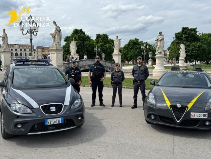 GdF Padova Five Guardia di Finanza officers stand between two patrol cars in a plaza with statues and trees in the background.