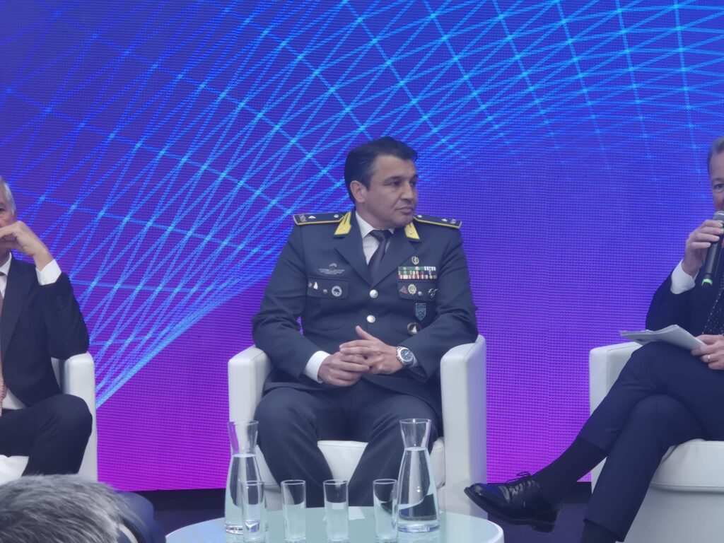 Gioco illegale generale Esposito Guardia di Finanza | AGIMEG Panel of men seated on stage; central figure in military uniform with medals, speaking into a mic against a blue geometric backdrop