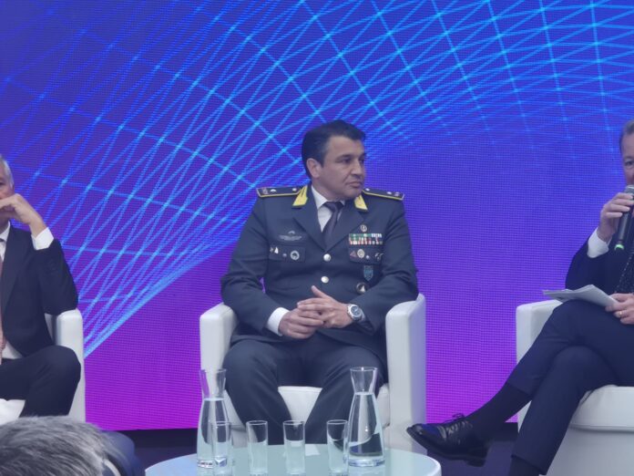 Gioco illegale generale Esposito Guardia di Finanza Panel of men seated on stage; central figure in military uniform with medals, speaking into a mic against a blue geometric backdrop