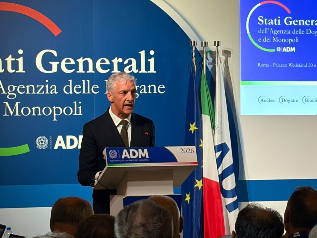 Man in a suit speaking at a podium with ADM logo, blue backdrop and flags behind him