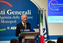 Stati Generali ADM, Mazzella (Dir. Relazioni Internazionali): “Centrale il nuovo Data Hub europeo”. Oliviero (Dir. Dogane): “Nuova riforma si inserisce in un periodo storico molto complesso” Man in a suit speaking at a podium with ADM logo, blue backdrop and flags behind him