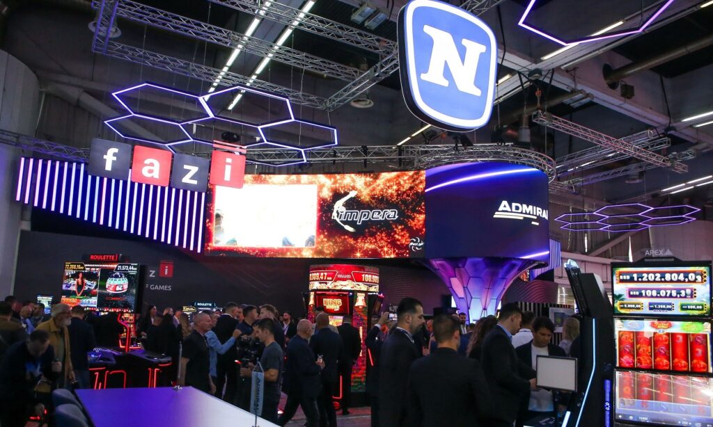 Large 'fazi' signage hangs above a crowded exhibition booth with purple neon hex lights and big screens overhead.