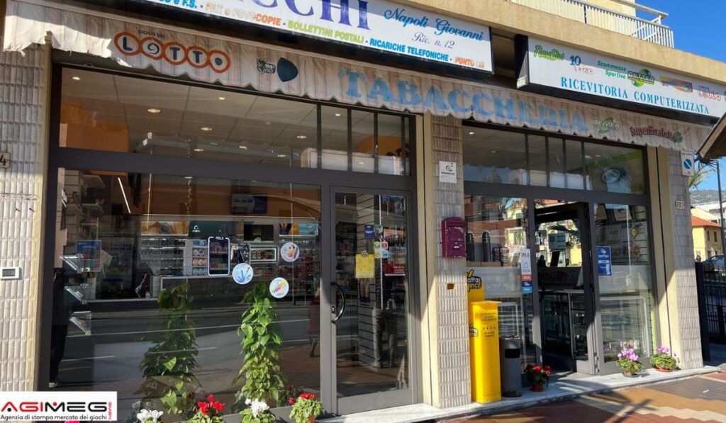 Glass-front tobacconist shop with a large 'TABACCHERIA' sign, storefront plants, and a yellow newspaper stand outside.