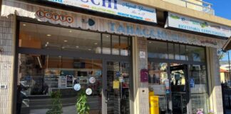 MillionDay: vinto un milione di euro a Loano (Savona). Il titolare della tabaccheria: “Non ci aspettavamo una vincita così” Glass-front tobacconist shop with a large 'TABACCHERIA' sign, storefront plants, and a yellow newspaper stand outside.
