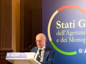 Sergio Gallo Direttore Antifrode dellAgenzia delle Dogane e dei Monopoli | AGIMEG Older man in a suit speaks at a podium during a conference, ADM banner visible behind him.