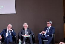 Silvestri (dir. Scuola Italiana Antiriciclaggio): “Gioco pubblico ha un ruolo importante sul piano dell’informazione ed è presidio di legalità” Three men in dark suits seated on a panel stage, engaged in a discussion at a conference.