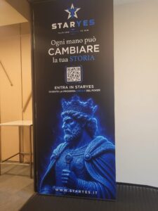 Staryes Battle of Malta | AGIMEG Tall STARYES banner with logo, Italian slogan 'Ogni mano può cambiare la tua storia', QR code and a blue statue image at the bottom.