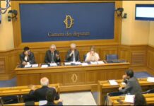 Linee guida AGCOM per campagne di comunicazione contro la ludopatia: Alea, Assoutenti e Forum Famiglie presentano osservazioni alla Camera Panel of four officials seated at a long raised desk in a parliamentary chamber, blue backdrop reading 'Camera dei deputati' behind them with an emblem above the desk.