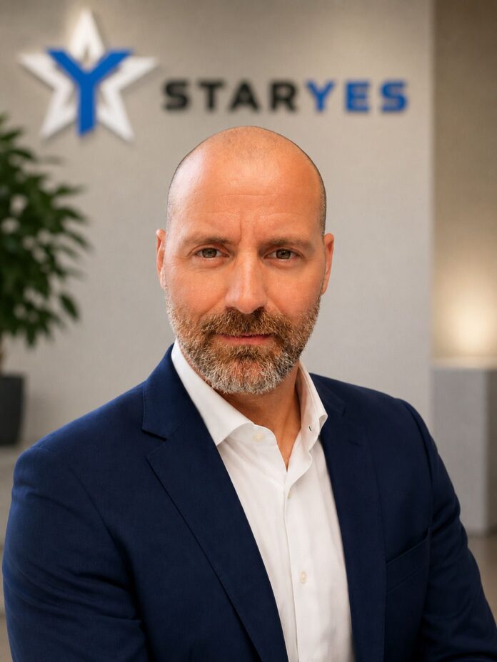 Angelo Merola AD Staryes Professional headshot of a bald man with a gray beard in a navy suit and white shirt, in front of a STARYES sign.