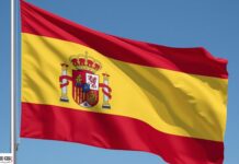 Scommesse illegali e tutela dei minori: la Spagna vara un nuovo piano di azione Spanish flag waving in the wind against a clear blue sky, showing red-yellow-red stripes and the national coat of arms in the center of the yellow band.