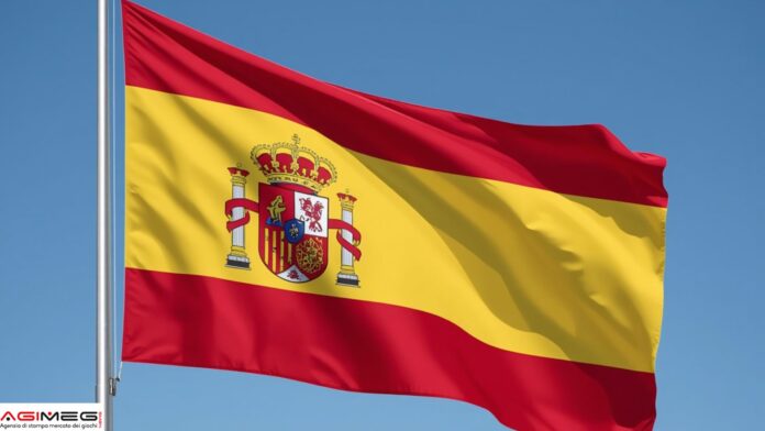 Bandiera Spagna Spanish flag waving in the wind against a clear blue sky, showing red-yellow-red stripes and the national coat of arms in the center of the yellow band.