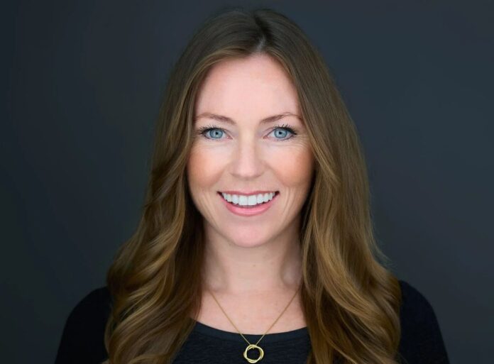 Mallory Reynolds-Trout IGB Live Smiling woman with blue eyes and long light brown hair against a dark gray background.