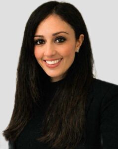 Marzia Aletta - Lottery Director Sisal | AGIMEG Professional headshot of a smiling woman with long dark hair wearing a black top against a light background, conveying a friendly, approachable vibe.