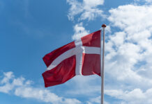 Antiriciclaggio: in Danimarca obbligo di valutazione del rischio per le nuove tecnologie nel settore del gioco Danish flag (red with a white cross) waving on a flagpole against a blue sky with clouds in the background.