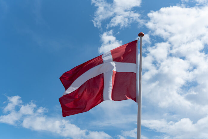 Copenhagen - Denmark - July 4 - 2023 - Denmark Flag Danish flag (red with a white cross) waving on a flagpole against a blue sky with clouds in the background.