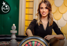 Casinò online: colpo da 200.250 euro su Domusbet grazie alla Roulette Green Live di Pragmatic Play Female game show host sits at a roulette table with a visible roulette wheel, promotional 'Roulette Green' banner in the foreground.